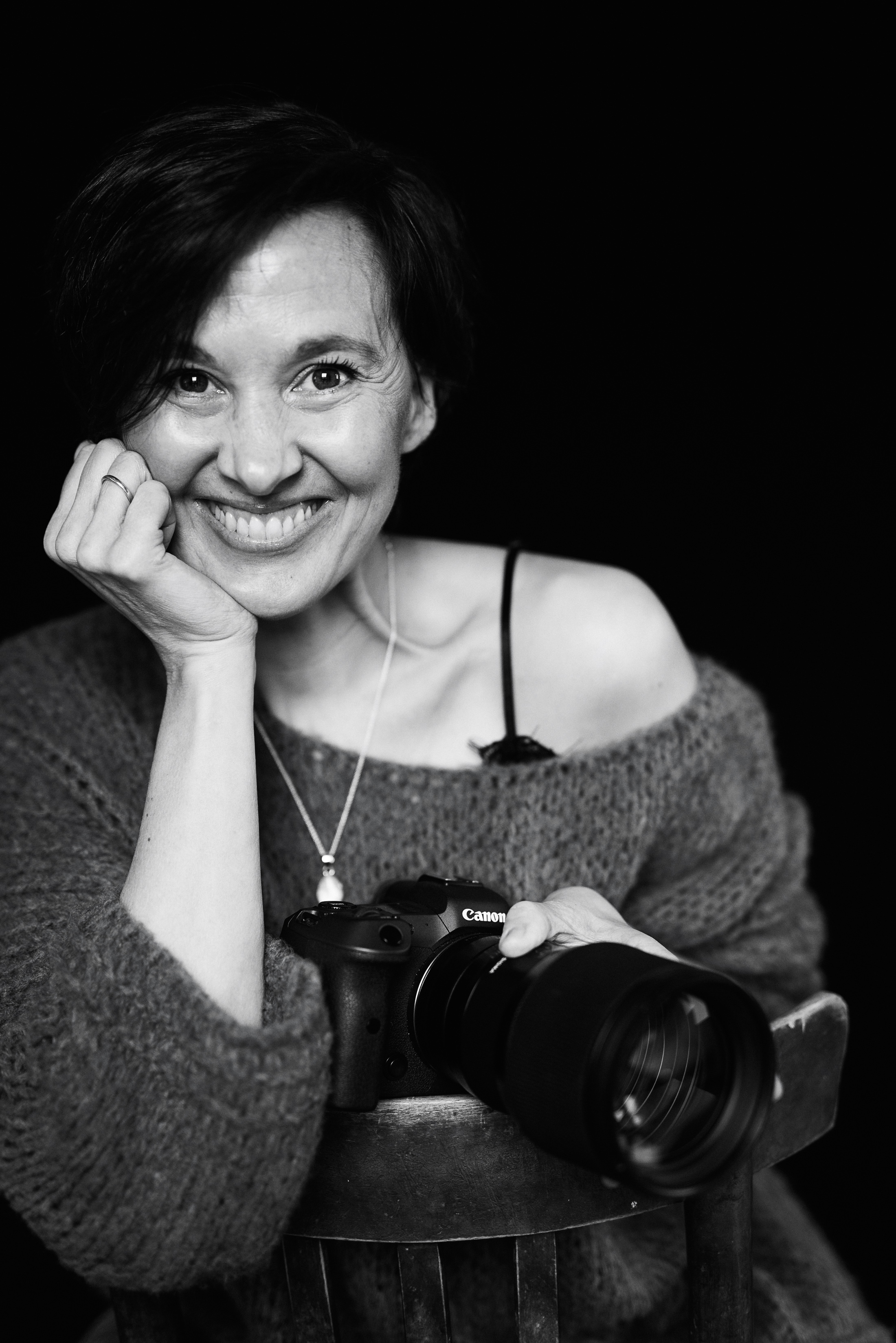 Ein Portrait von Nadine Wisser wie Sie den Kopf auf Ihrer Hand abstützt und lächelt. Im Vordergrund ist eine Kamera zu sehen.