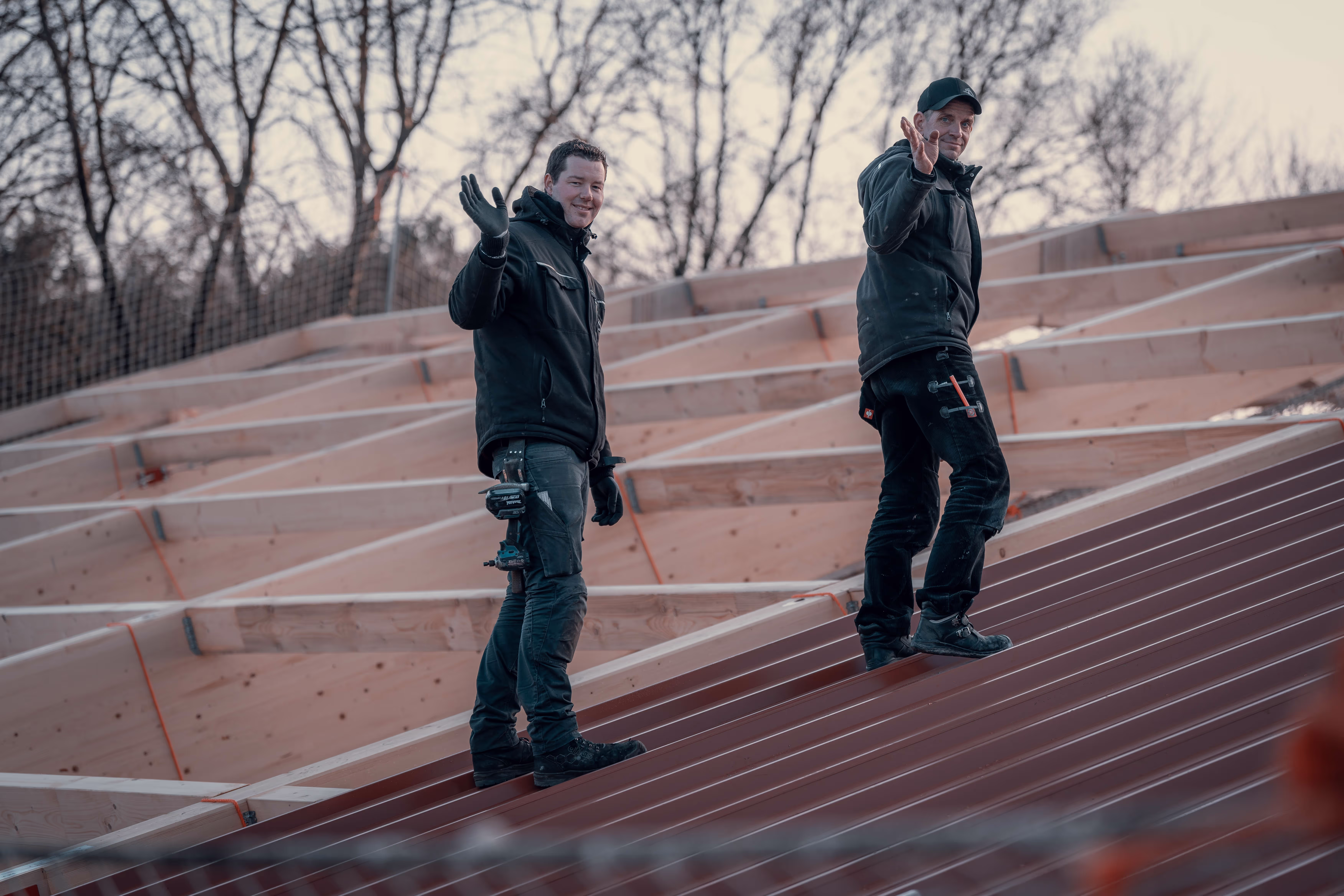 Zwei Zimmerer auf dem Dach winken | Teamarbeit und Freude am Holzbau
