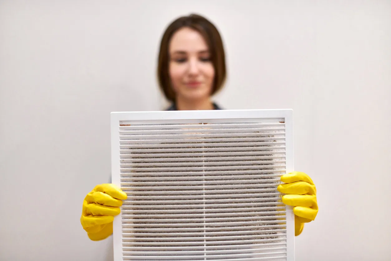 A person wearing yellow gloves holds a clean pleated air filter