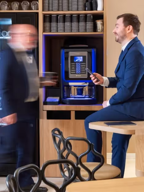 Two people around a coffee machine in a furnished business apartment, Yuna.