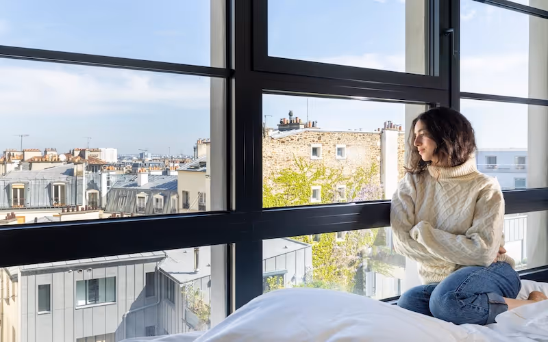Femme admirant la vue parisienne depuis sa chambre à Yuna Montmartre.