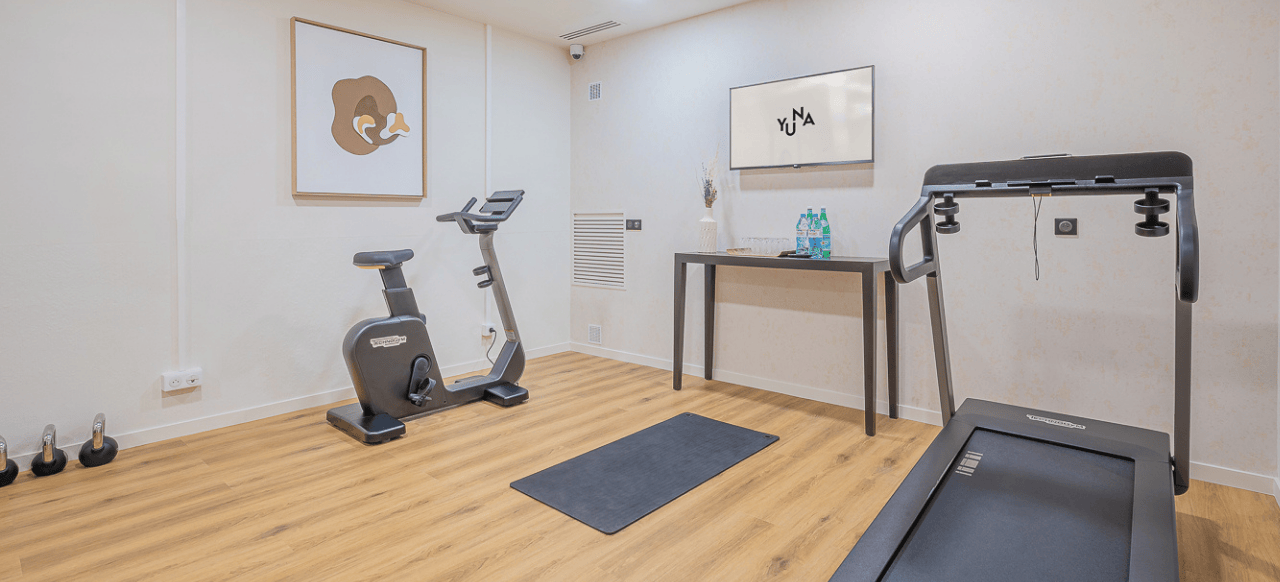 Salle de fitness moderne chez Yuna Porte Maillot, équipée de divers appareils d'exercice et bénéficiant d'une lumière naturelle.