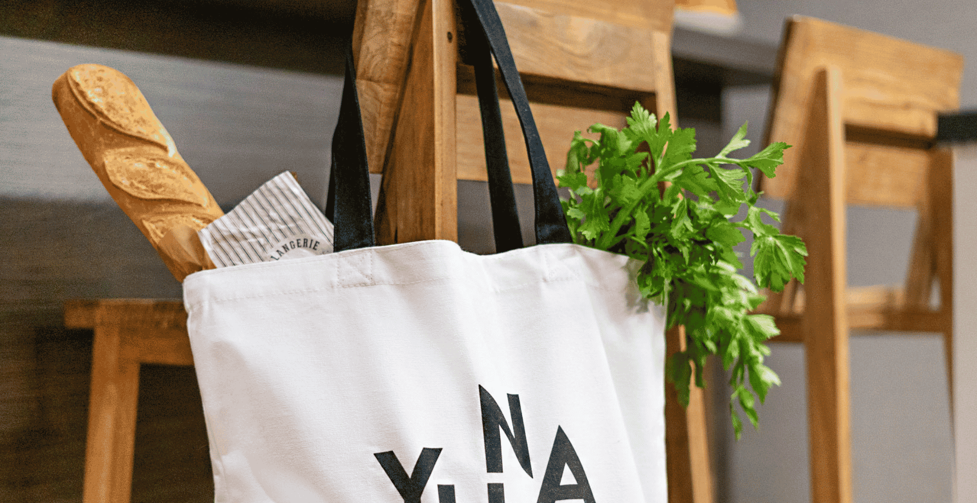 Gros plan d'un sac en toile blanc avec des anses noires suspendu à un escabeau en bois.