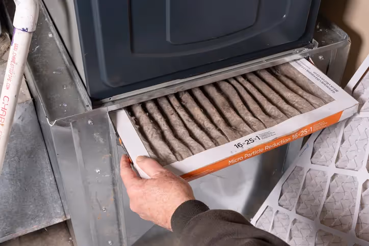 Person removing dirty air filter from HVAC system with visible debris