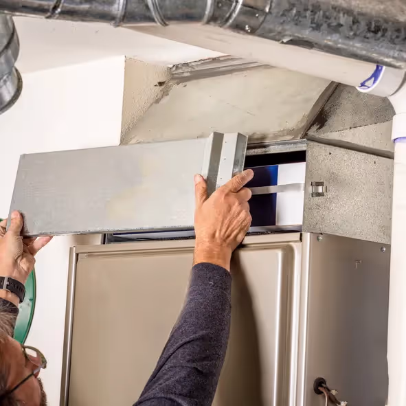 Person adjusting metal duct connected to furnace in HVAC system with surrounding pipes