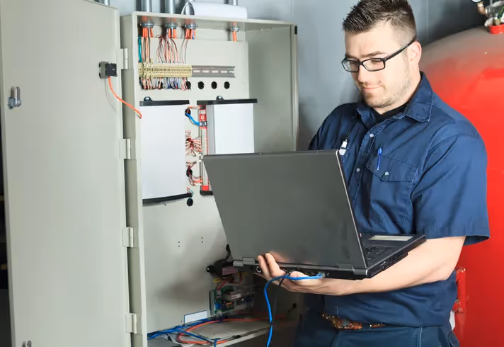 Person using laptop to work on electrical panel with visible wires and components