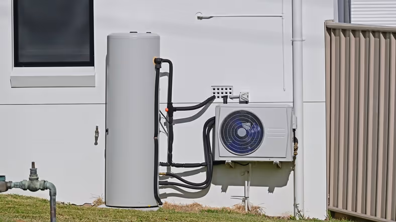Outdoor heat pump water heater system against a white wall.