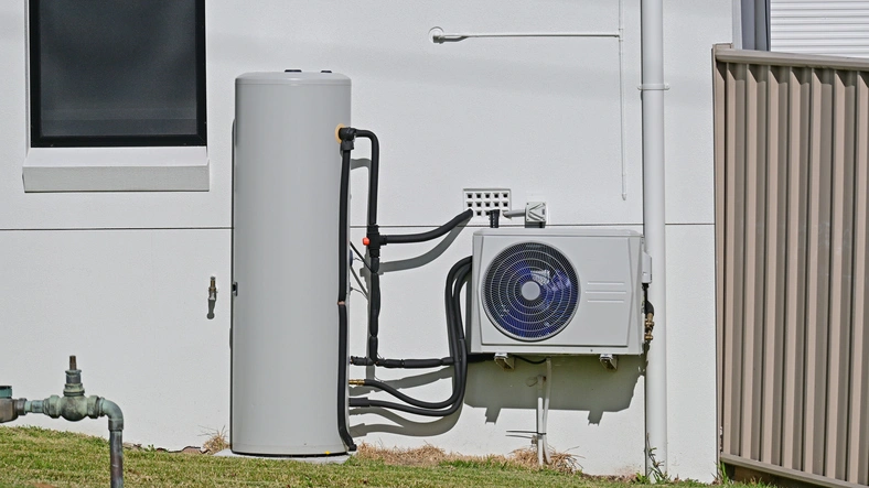 Outdoor heat pump water heater system against a white wall.