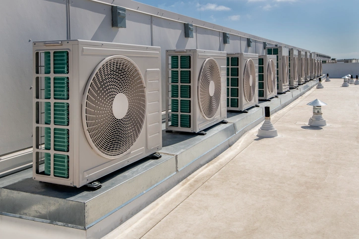 Row of large industrial air conditioning units on a flat rooftop under clear blue skies.