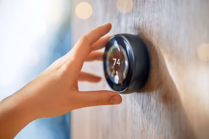 A hand adjusts a smart thermostat on a wooden wall, set to 74 degrees.