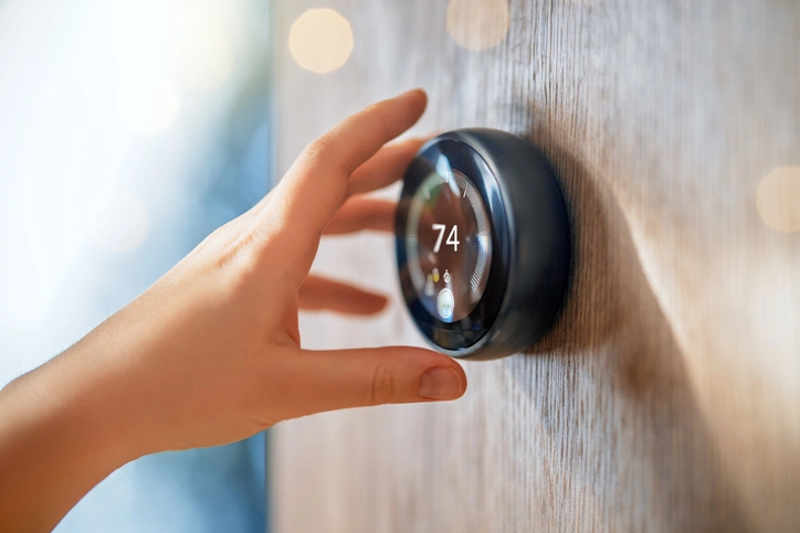 A hand adjusts a smart thermostat on a wooden wall, set to 74 degrees.