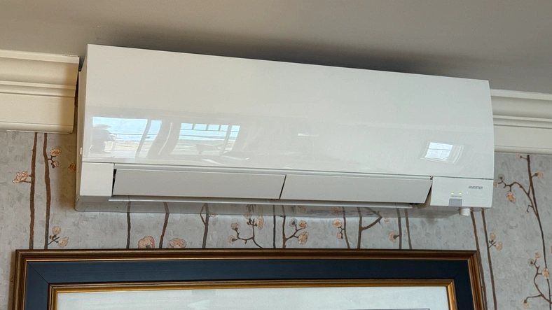A white wall-mounted air conditioner above a framed picture on floral wallpaper.