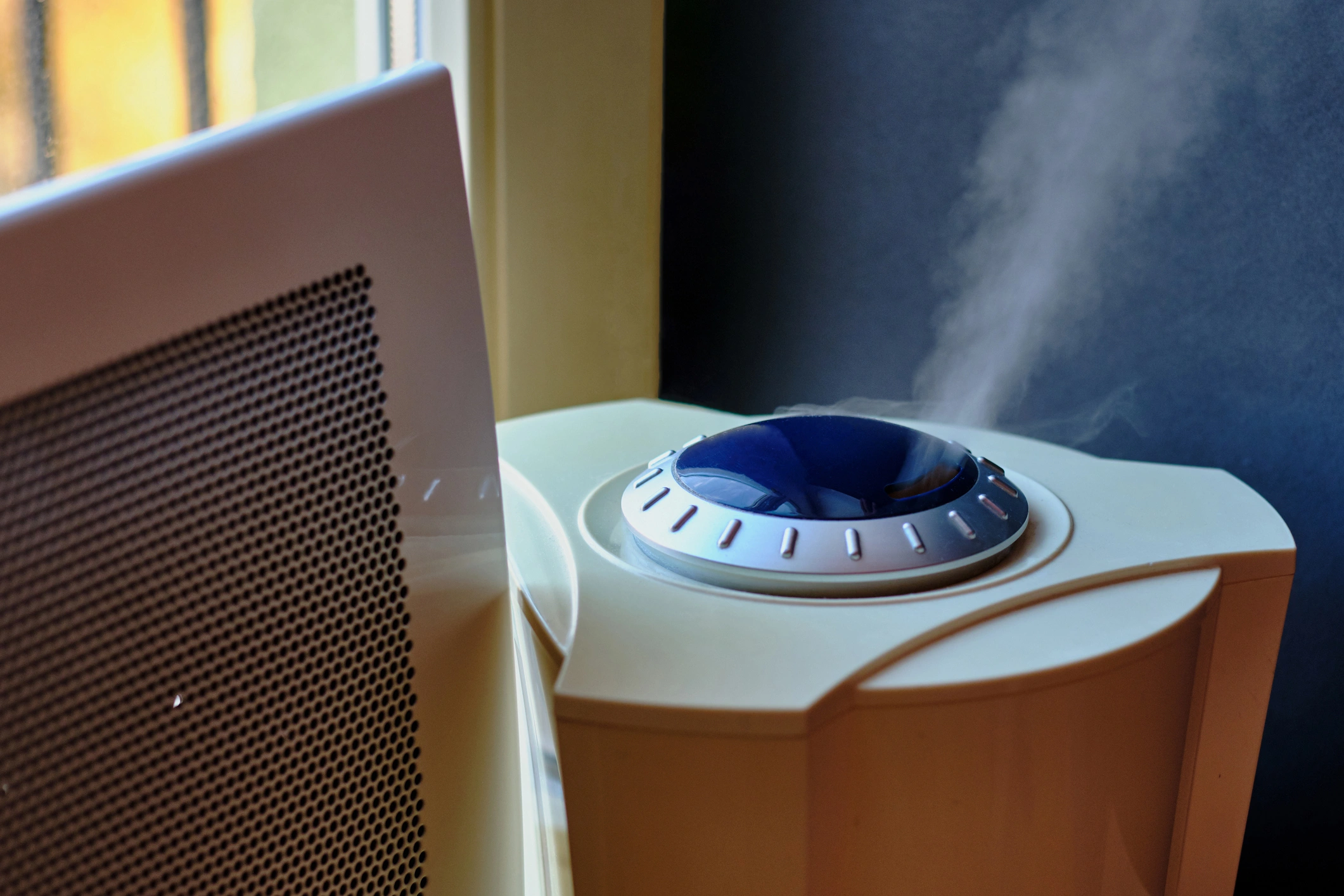 A white air purifier on a windowsill emits mist.
