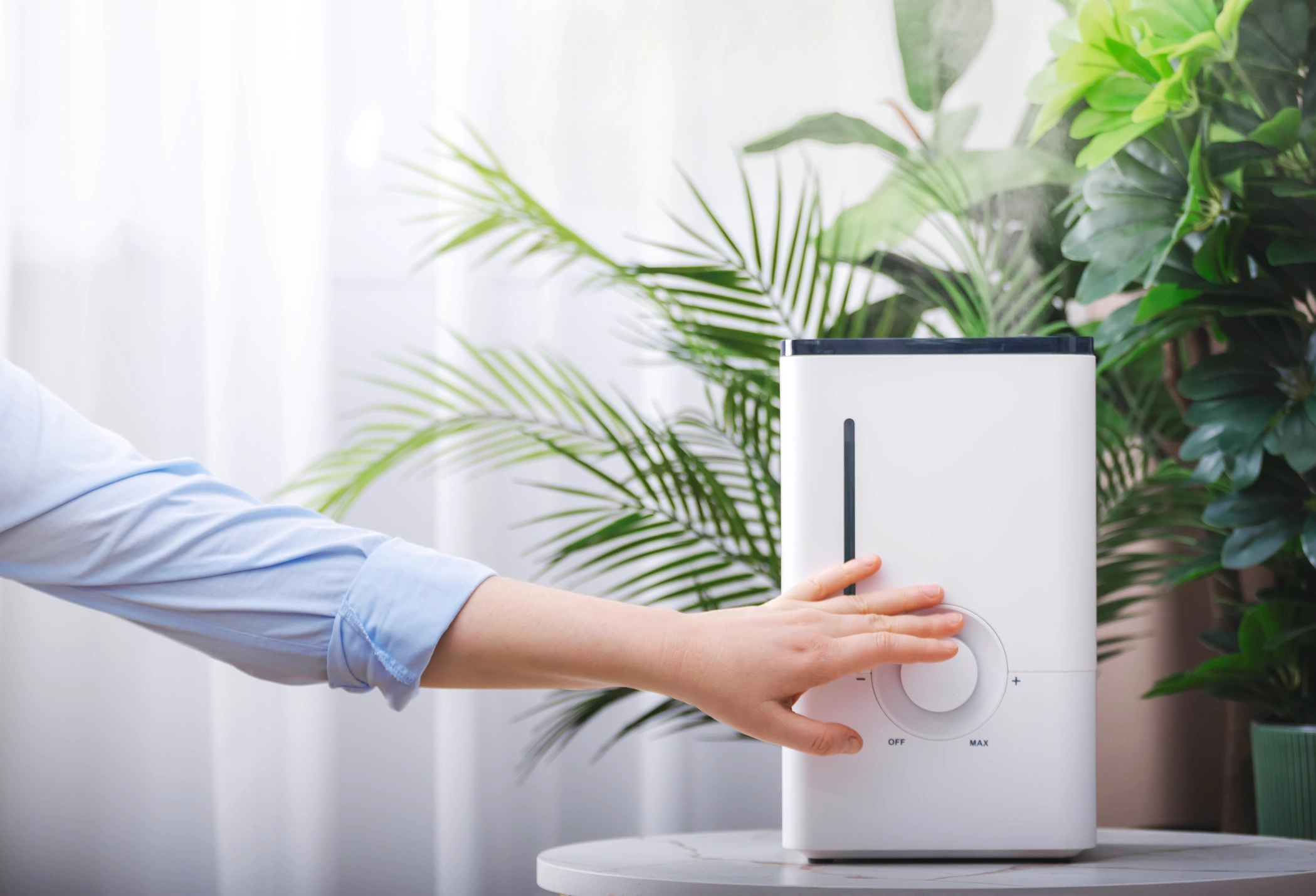 A person adjusts a white humidifier on a table