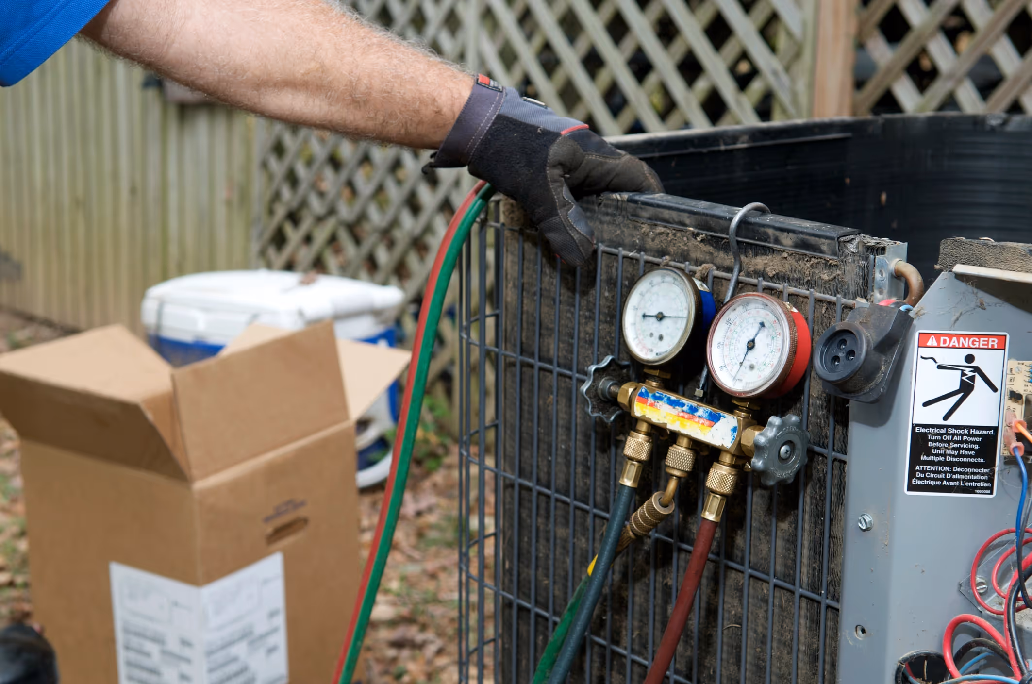Man wearing glove checks refrigerant gauges on an outdoor air conditioning unit.