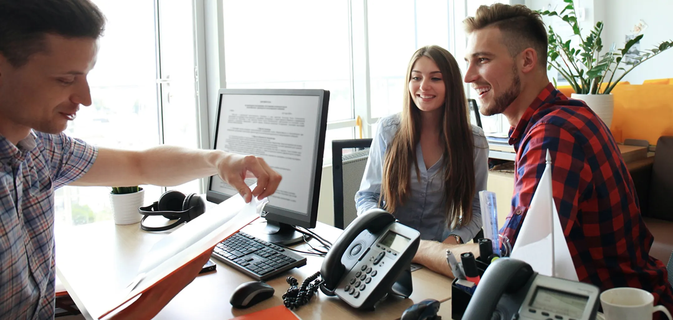 A group of three individuals collaborating at a desk with a computer.