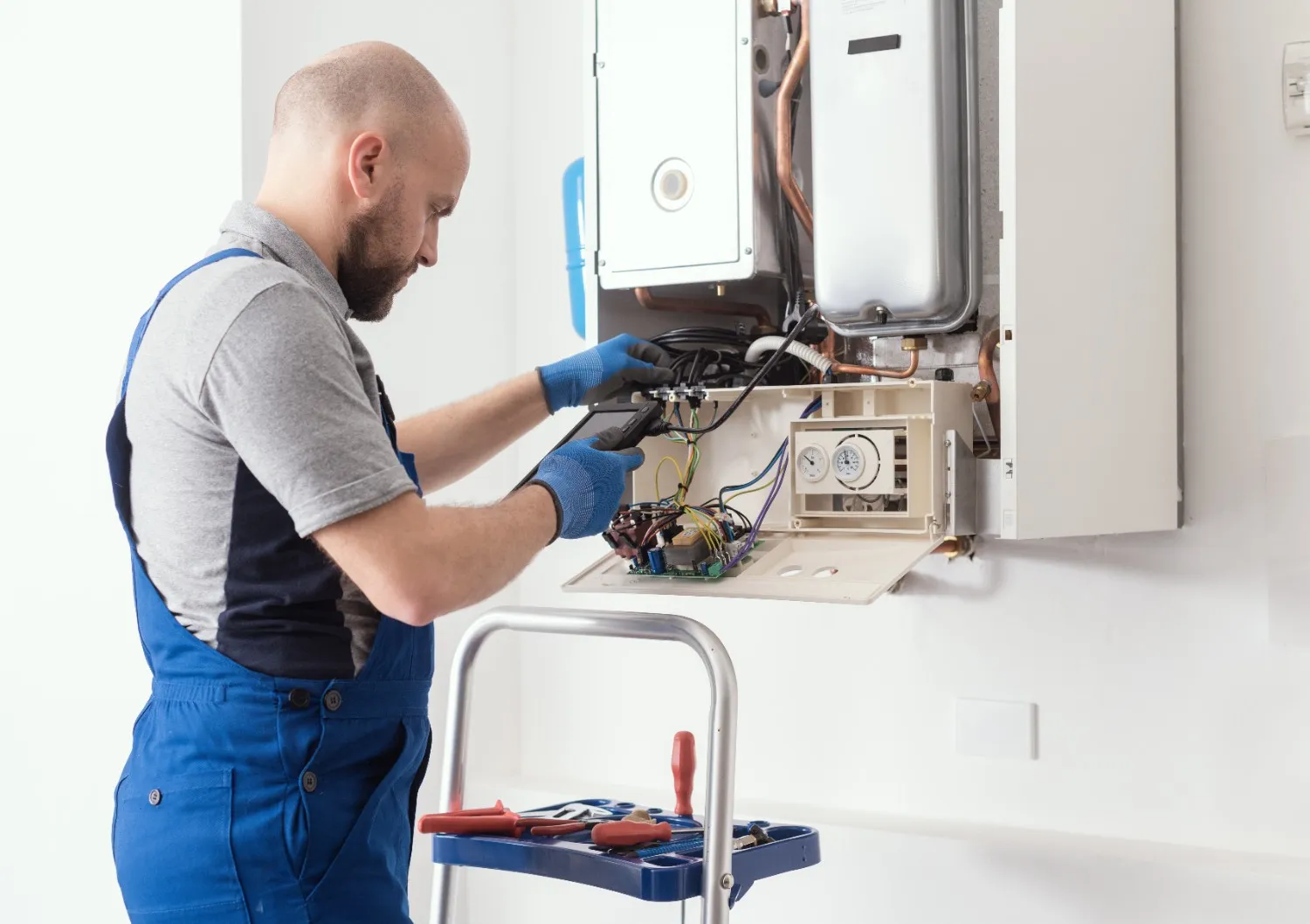 A plumber repairs a wall-mounted boiler.