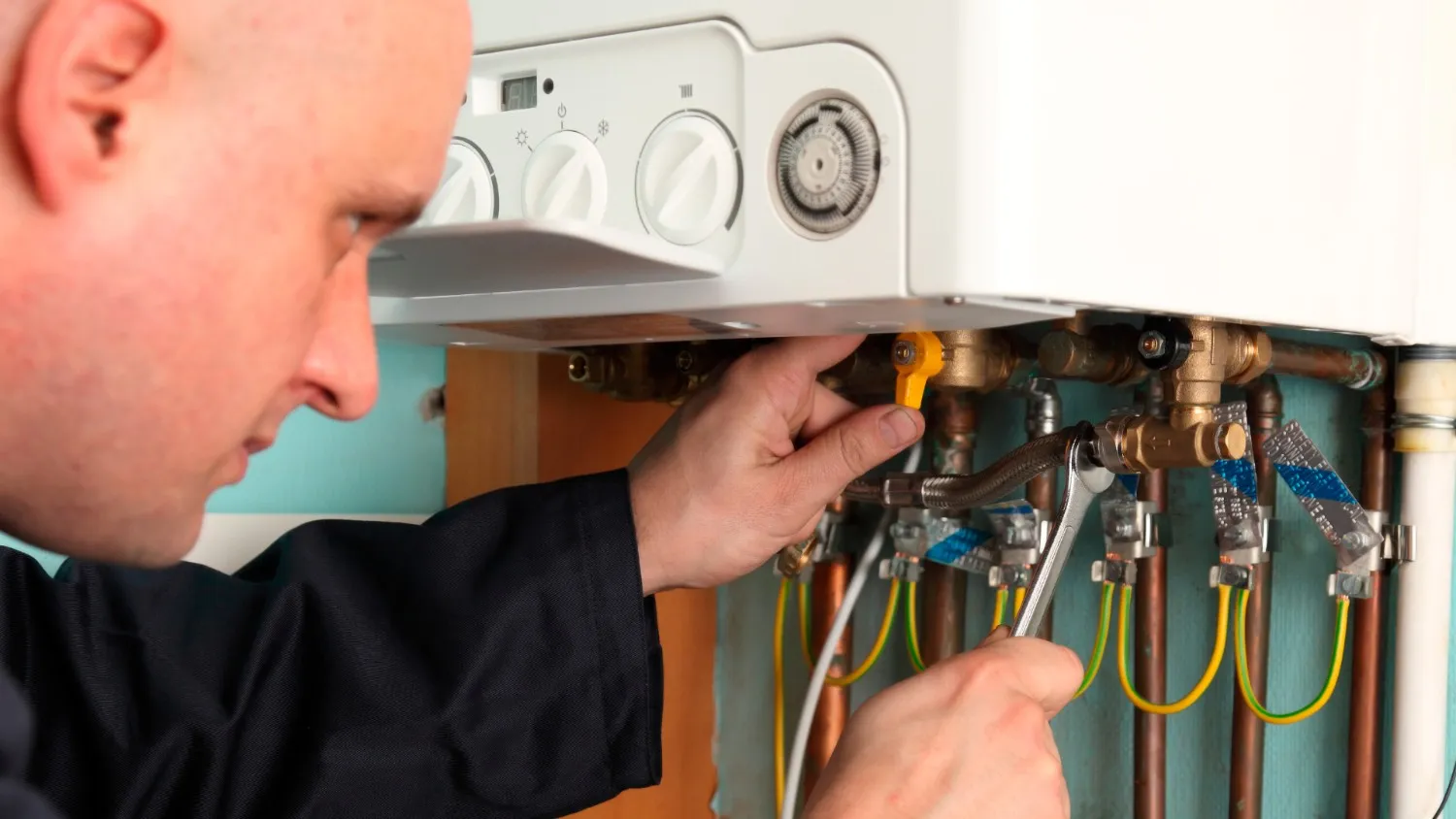 Plumber tightening pipes beneath a wall boiler.