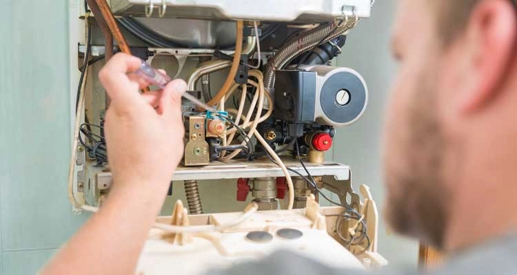 Technician adjusts boiler's internal components with screwdriver.