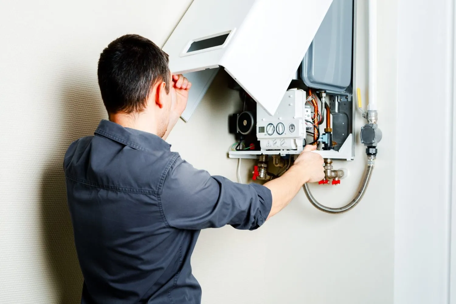Technician installing or repairing wall-mounted boiler unit.