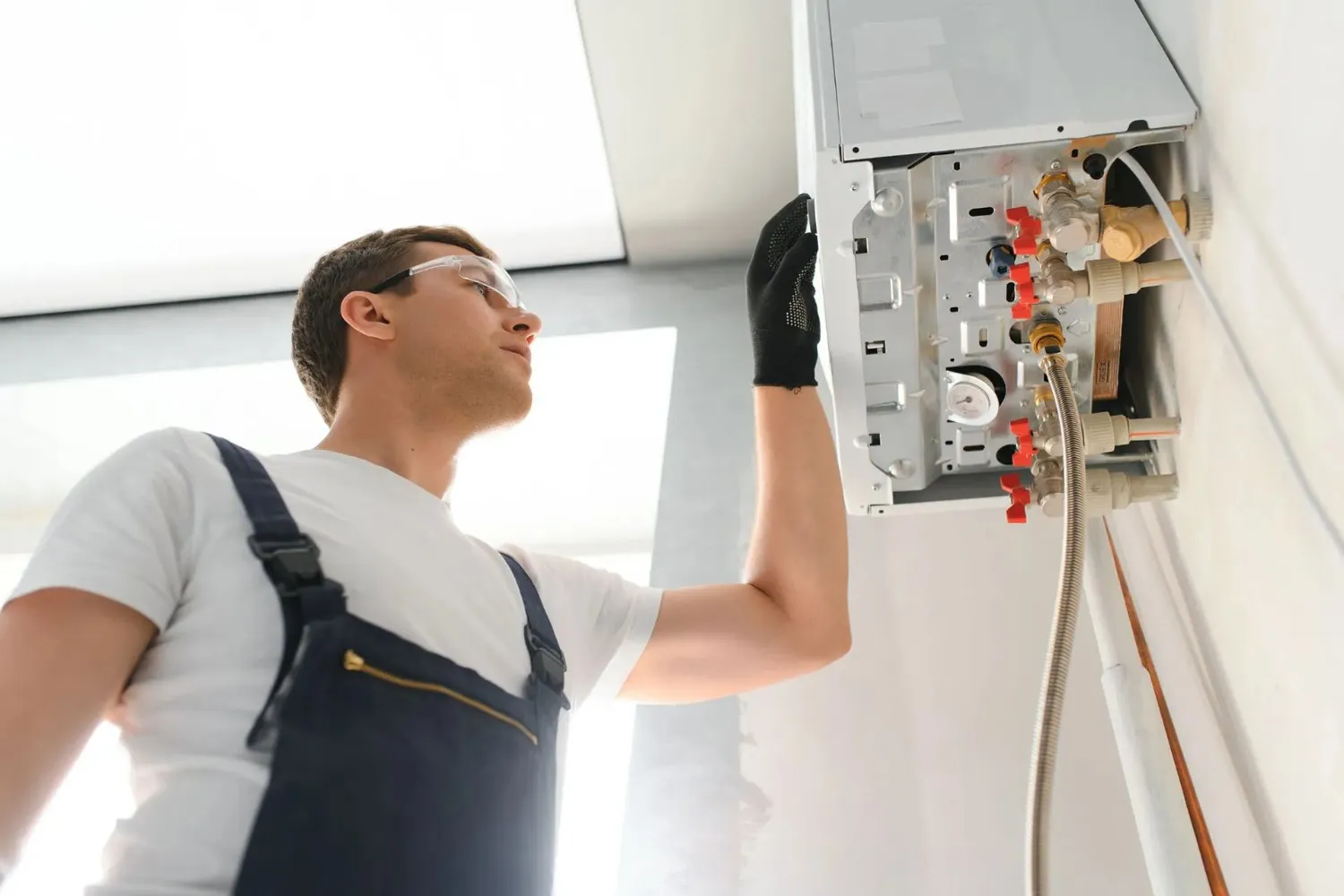 Technician in goggles inspecting open wall-mounted boiler.