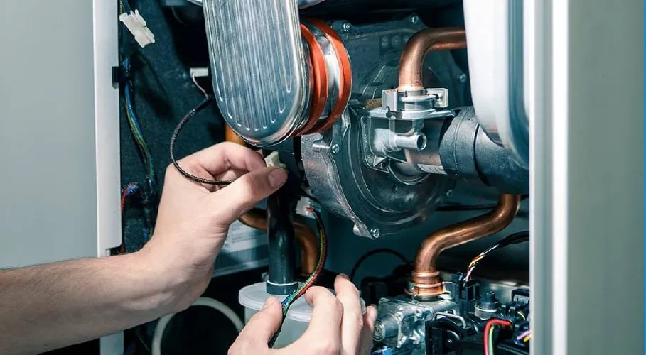 Hands connecting wiring inside open boiler.