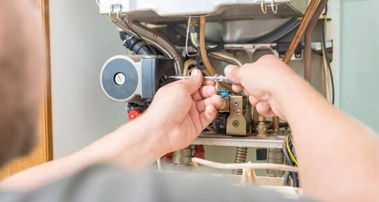 Repairman using screwdriver on boiler components.