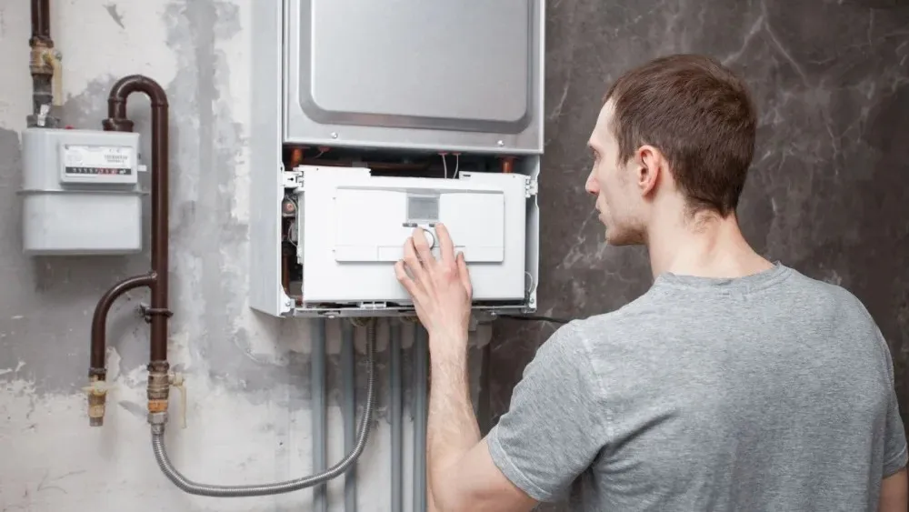 Man adjusting controls on wall-mounted boiler.