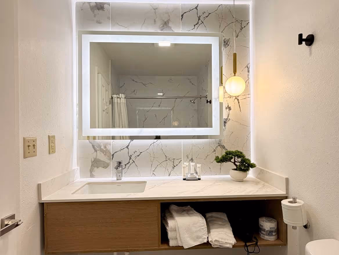 Modern bathroom vanity with white marble countertop, a rectangular illuminated mirror, a hanging globe light, and neatly folded towels underneath.