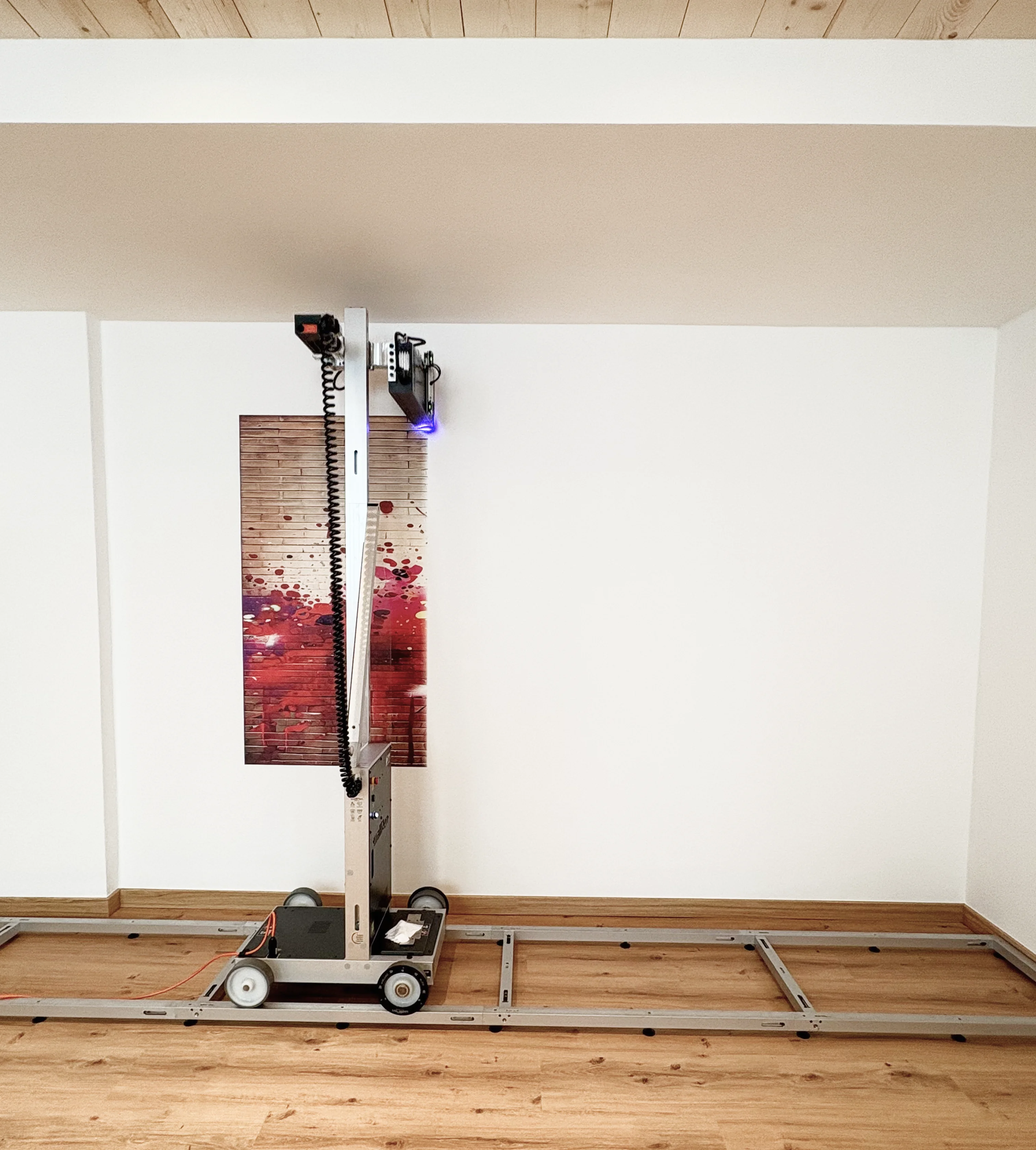 Ein platzierter Druckerroboter auf Schienen vor einer Wand mit einer bunten Holzlattengrafik.