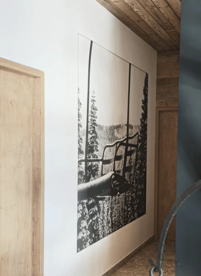 Schwarz-weiß Wandbild eines Sessellifts über bewaldeten Bergen in minimalistischem Raum mit Holztüren und Holzdecke.