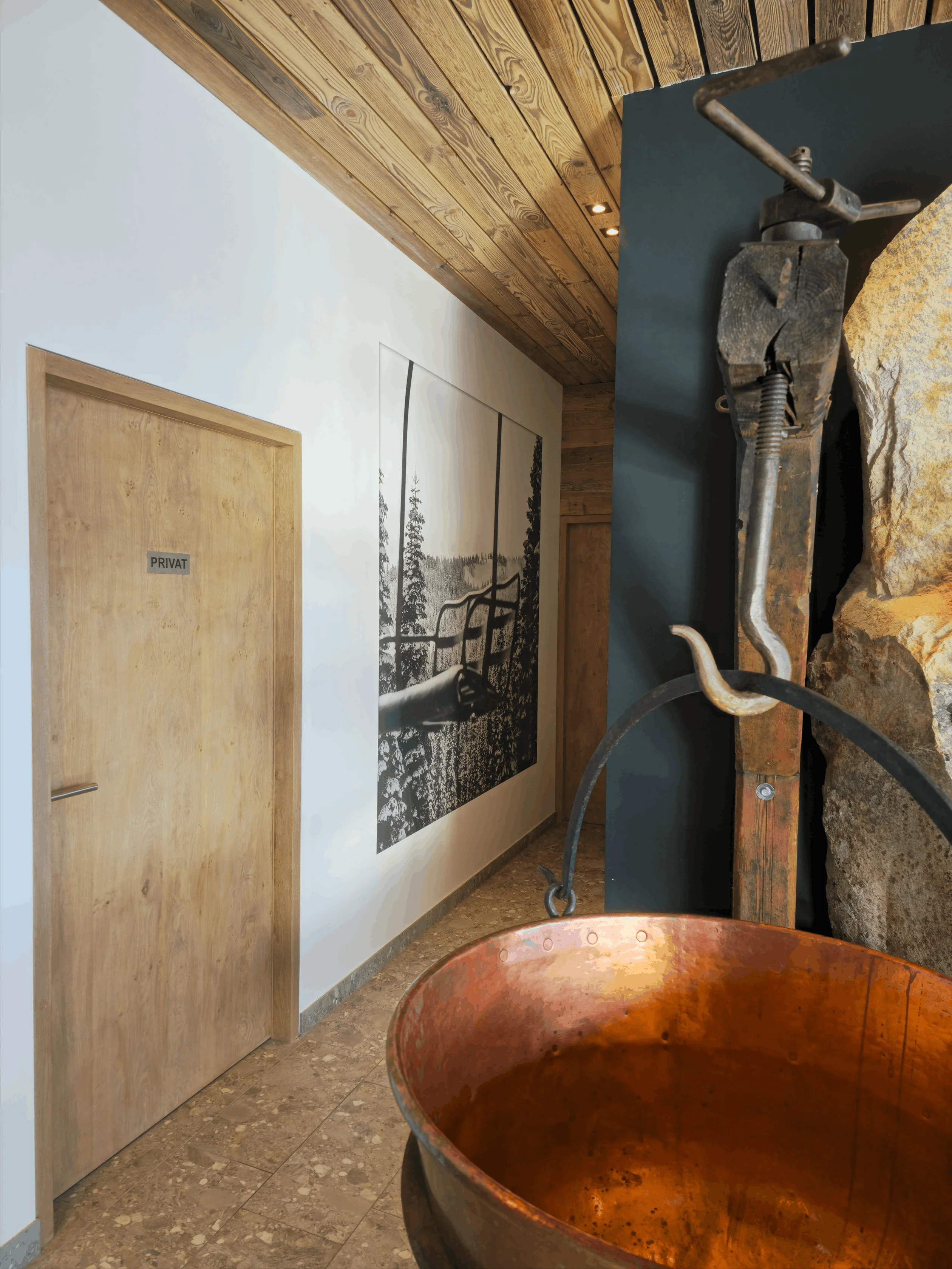 Innenraum mit Holztür mit Schild 'Privat', einem historischen mechanischen Gerät und einem großen Kupferkessel.
