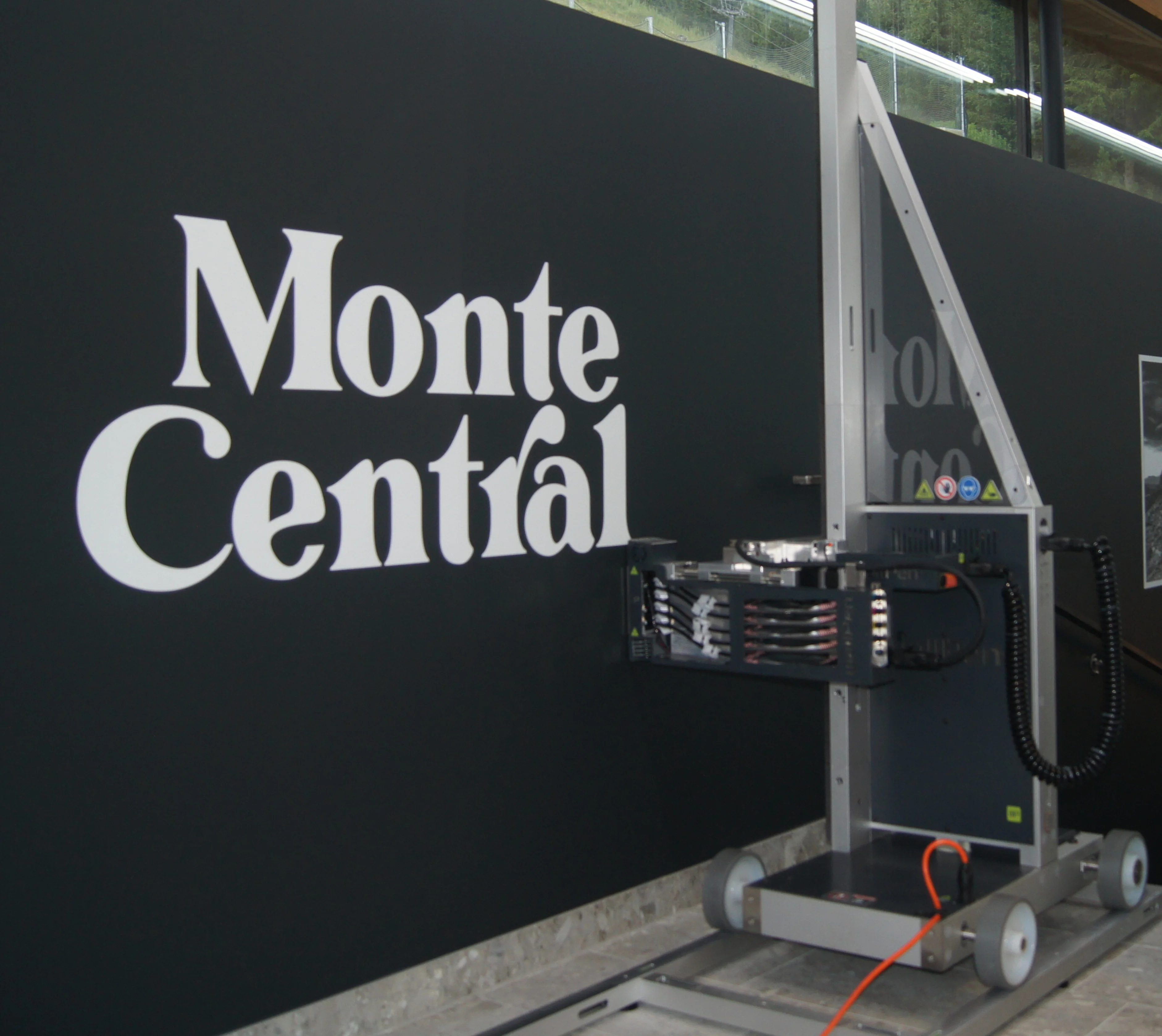 Druckmaschine druckt das weiße Logo Monte Central auf eine schwarze Wand.