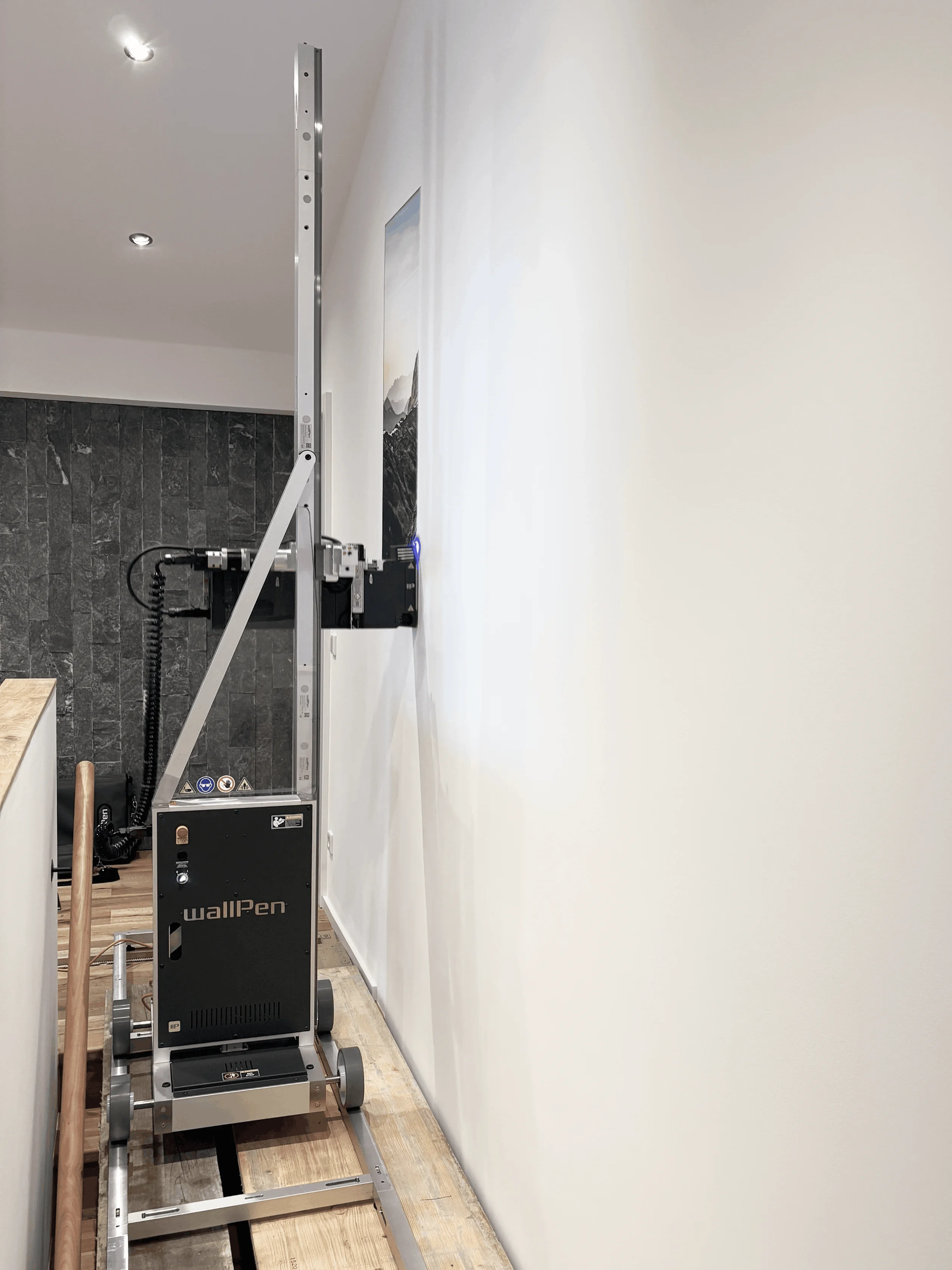 Automatischer Wanddrucker mit der Aufschrift „wallPen“, der ein Bild an eine helle Wand im Innenraum druckt.