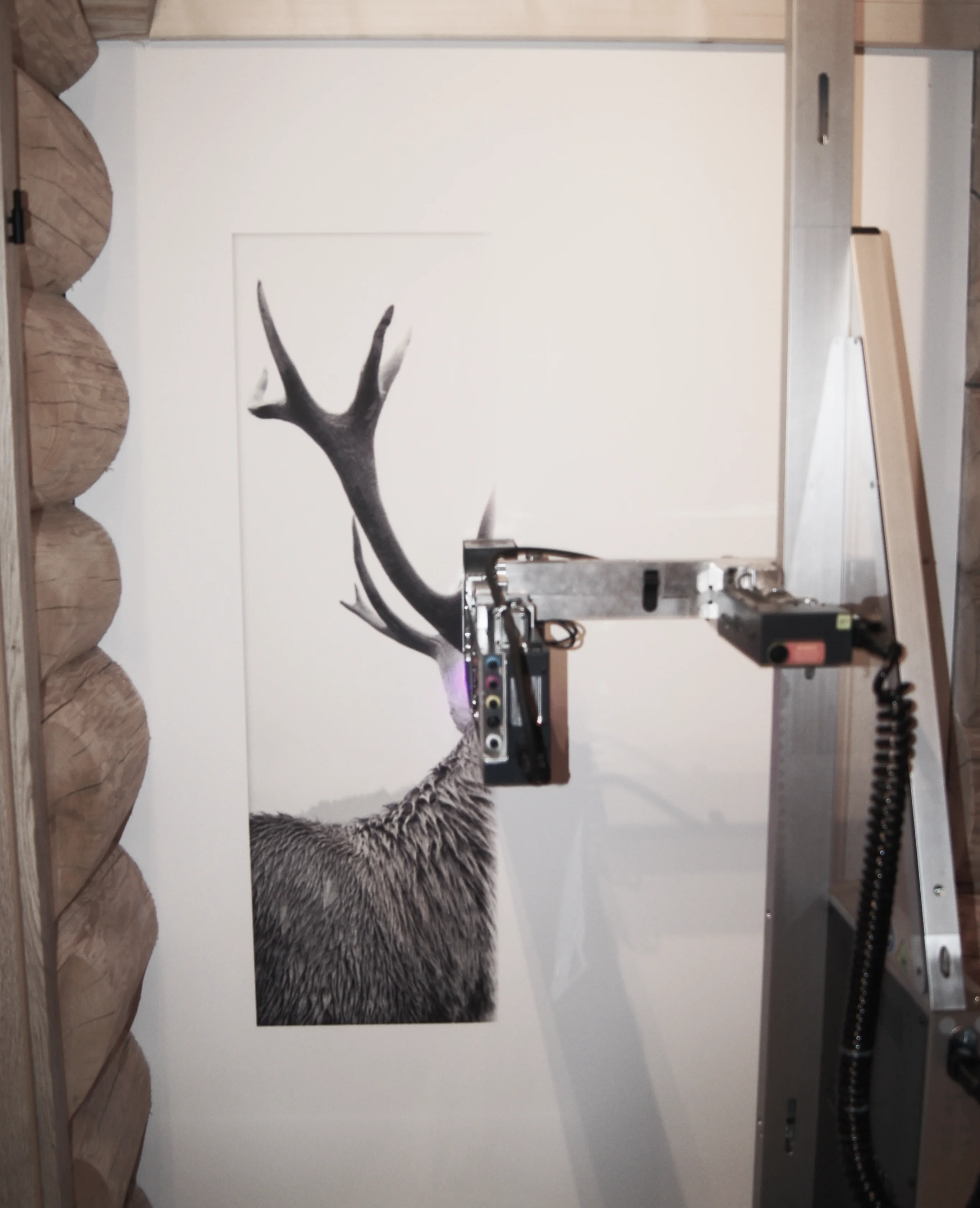 Automatische Druckmaschine bringt ein großes Schwarz-Weiß-Bild eines Hirschgeweihs und -körpers auf eine weiße Wand mit Holzstammverkleidung.
