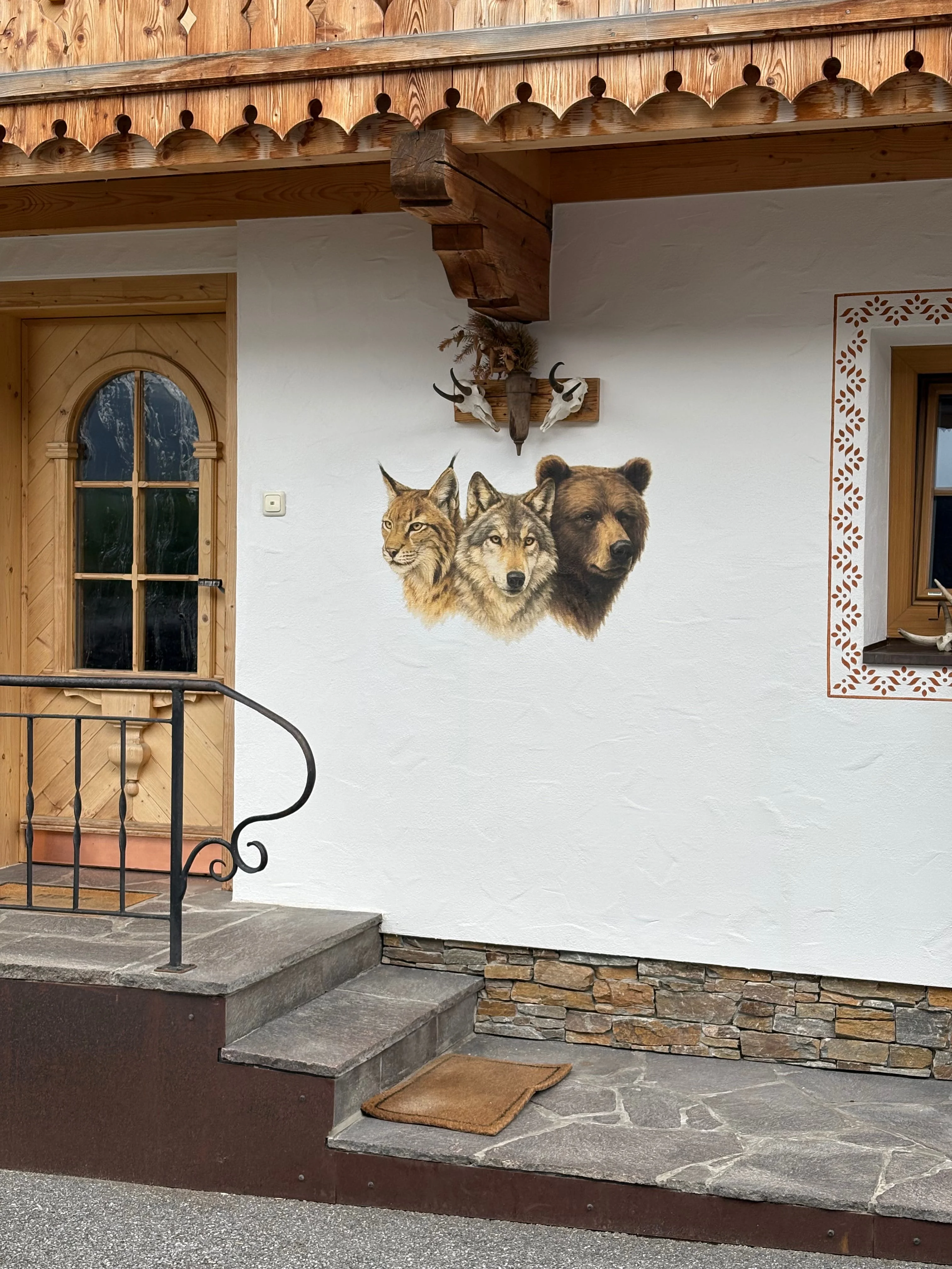 Hauswand mit bemaltem Bild von einem Luchs, Wolf und Bärenkopf und dekorativen Tierknochen über dem Bild.