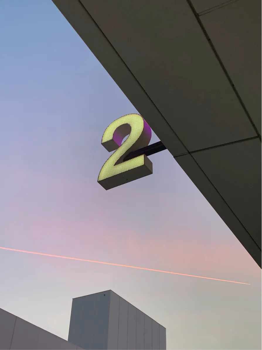 Gold number 2 sign on a building corner against a pink evening sky