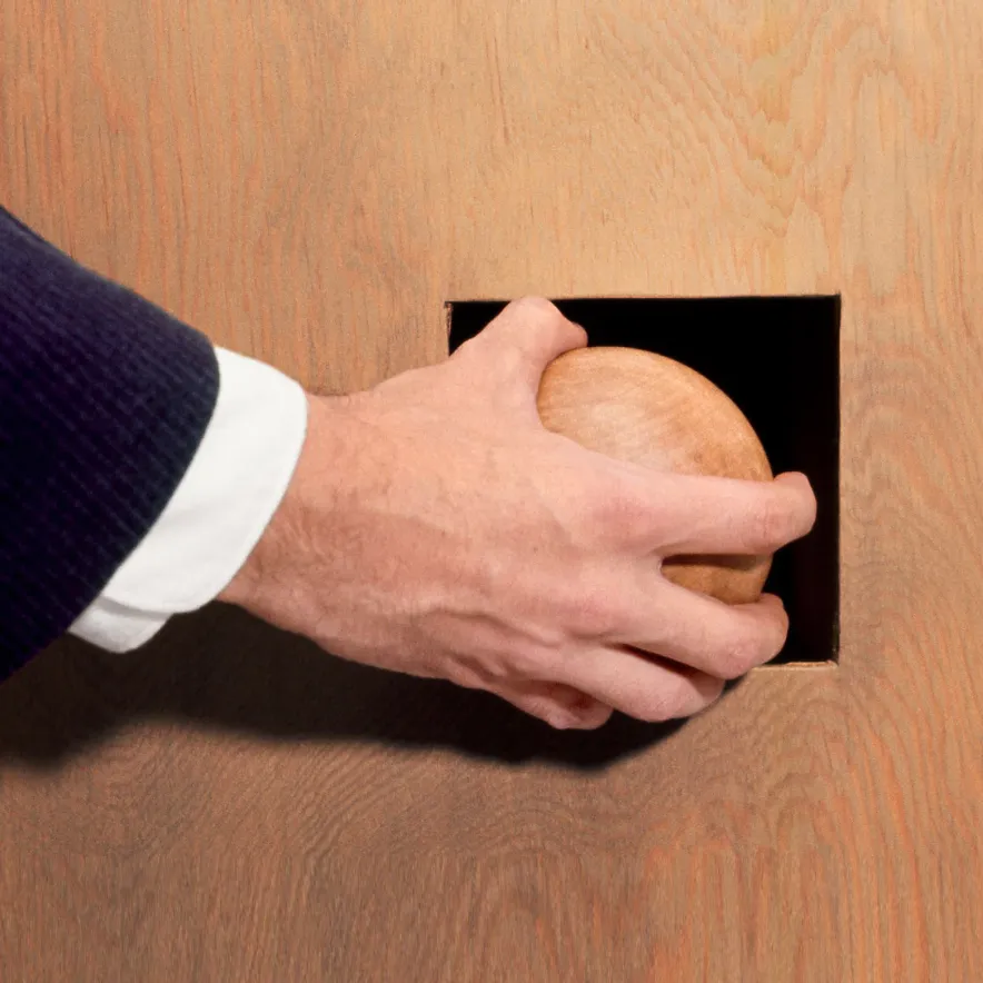 Hand in a suit sleeve reaching through a square opening in a wooden wall