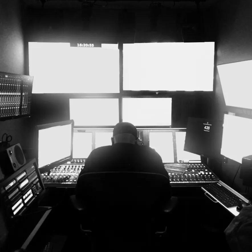 Person at an editing desk in front of bright monitors, in black and white