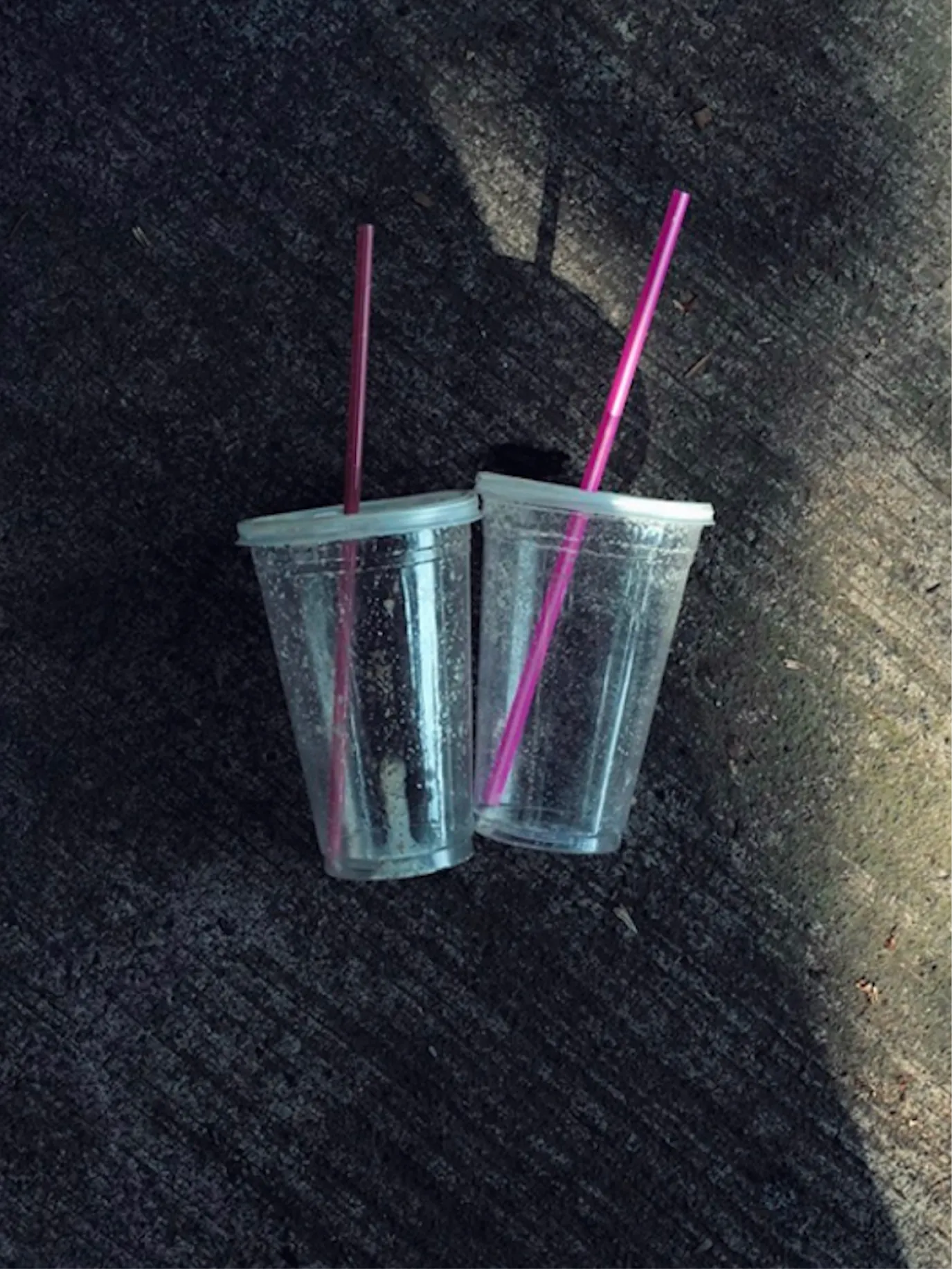 Two plastic cups with pink straws on dark asphalt
