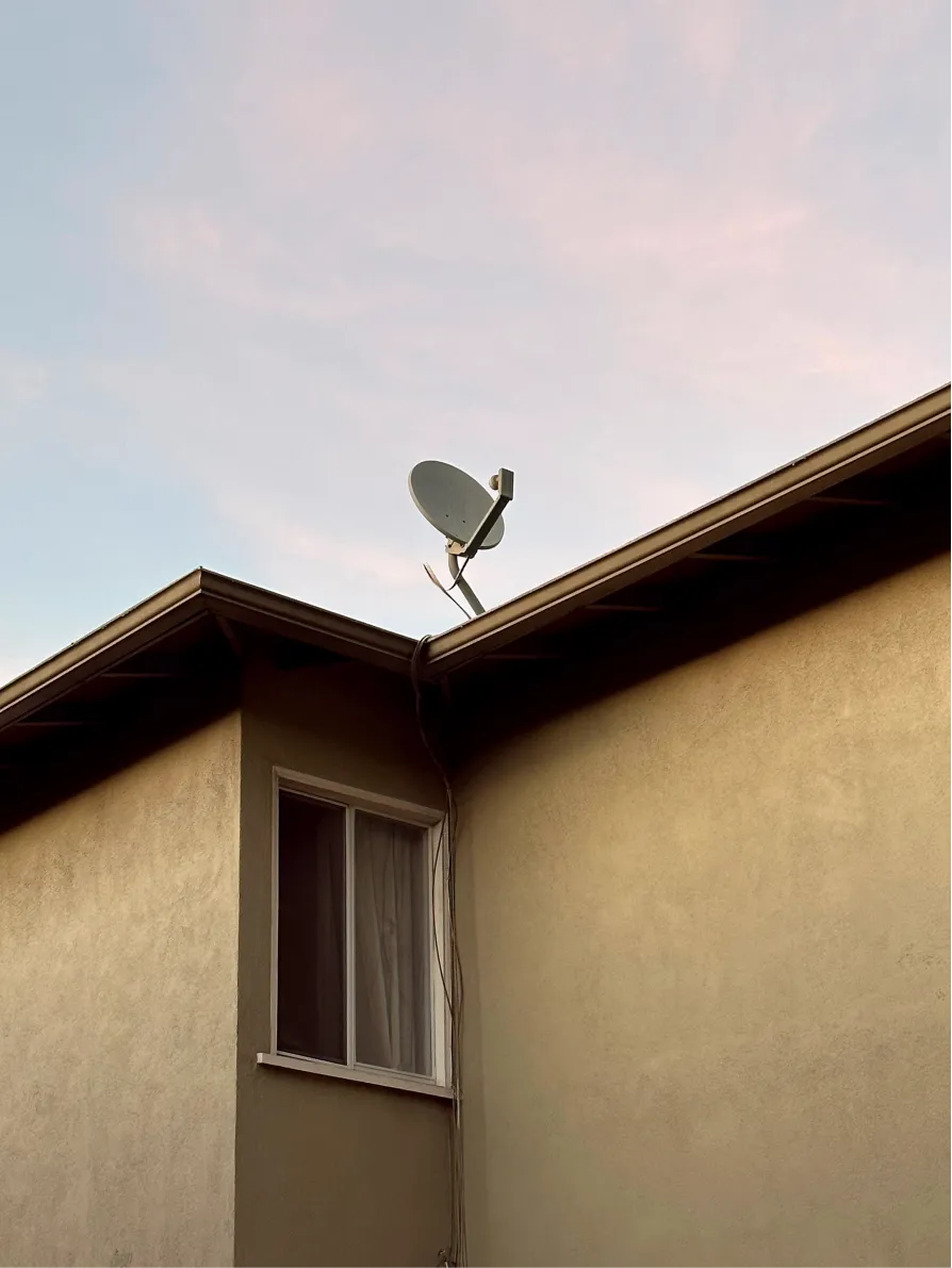 Corner of a house with a satellite dish against a pink sky