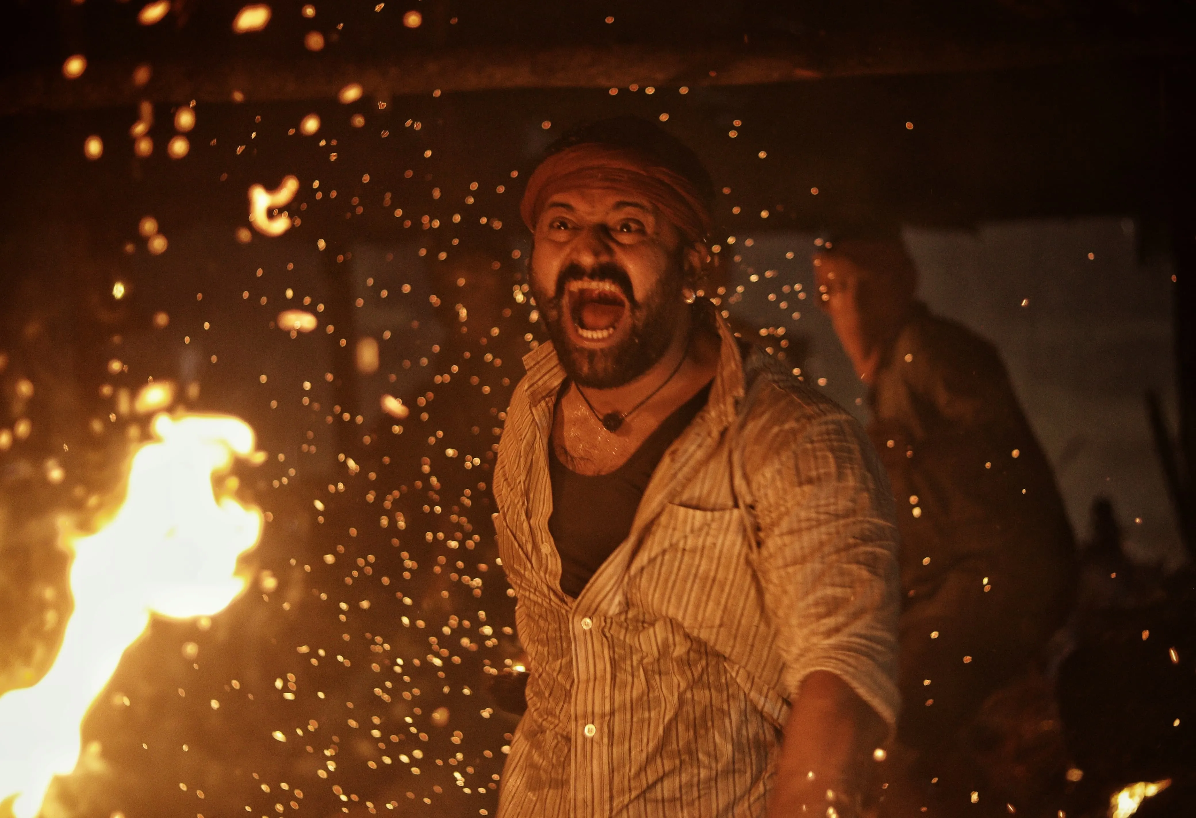 Screencrab from the movie Kanatara of a man holding a stick of fire beside him with an angry expressive emotion on his face 