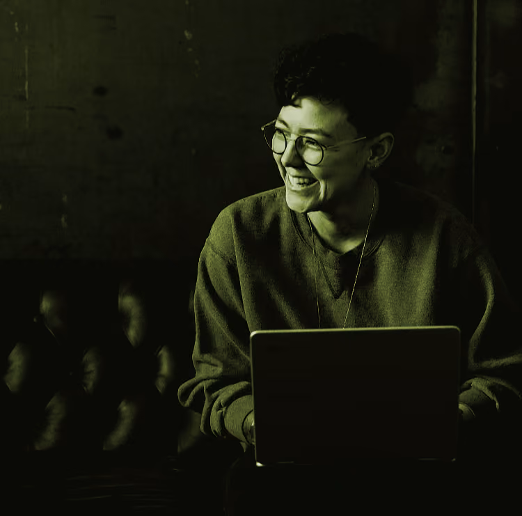 person sitting on a couch laughing holding a laptop
