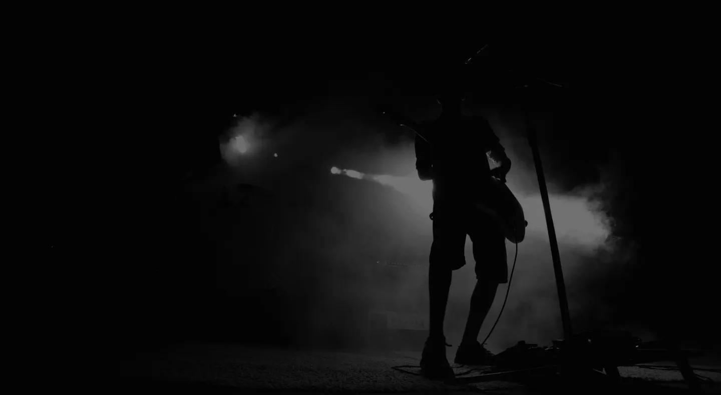 Silhouette of a guitarist performing on stage with bright backlight and fog effects.
