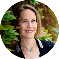 Porträt einer lächelnden Frau vor grünem Blätterhintergrund.