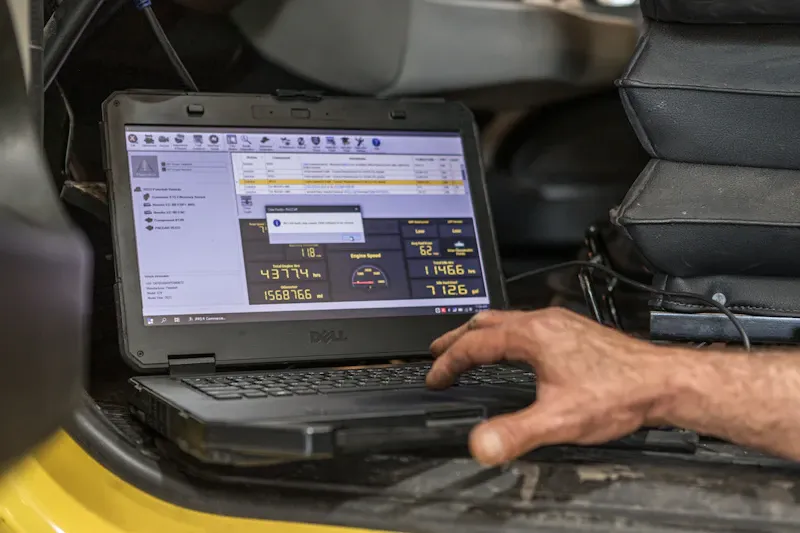 Technician performing heavy-duty diagnostic service using a Dell laptop with engine data displayed on the screen.