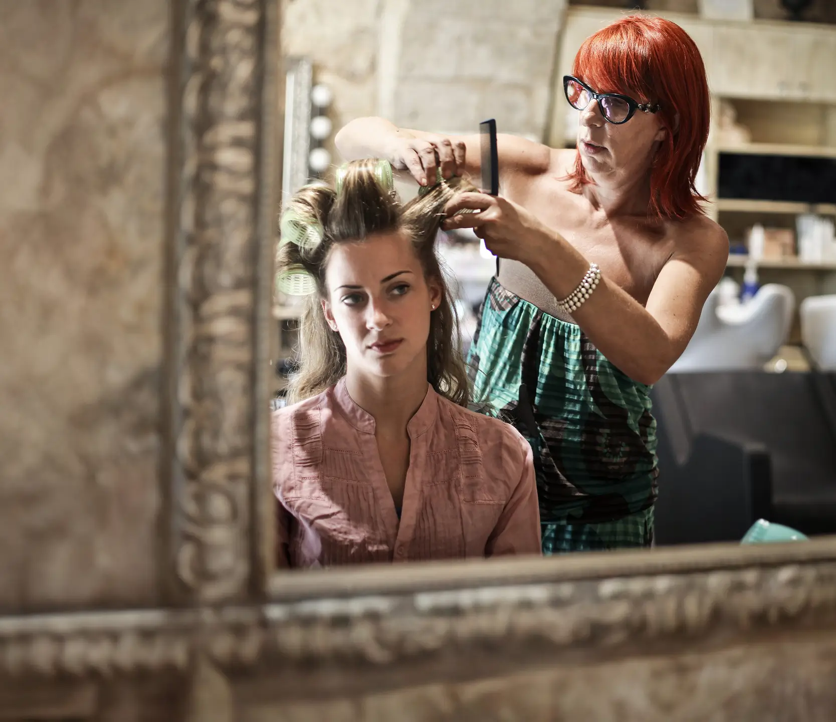 A hairstylist styles a client’s hair in front of a large salon mirror, focused and professional in a well-lit space.