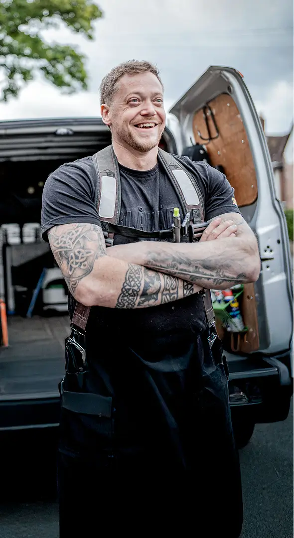 A confident tradesperson stands in front of an open van fully stocked with tools, smiling with arms crossed, ready for the day’s work.