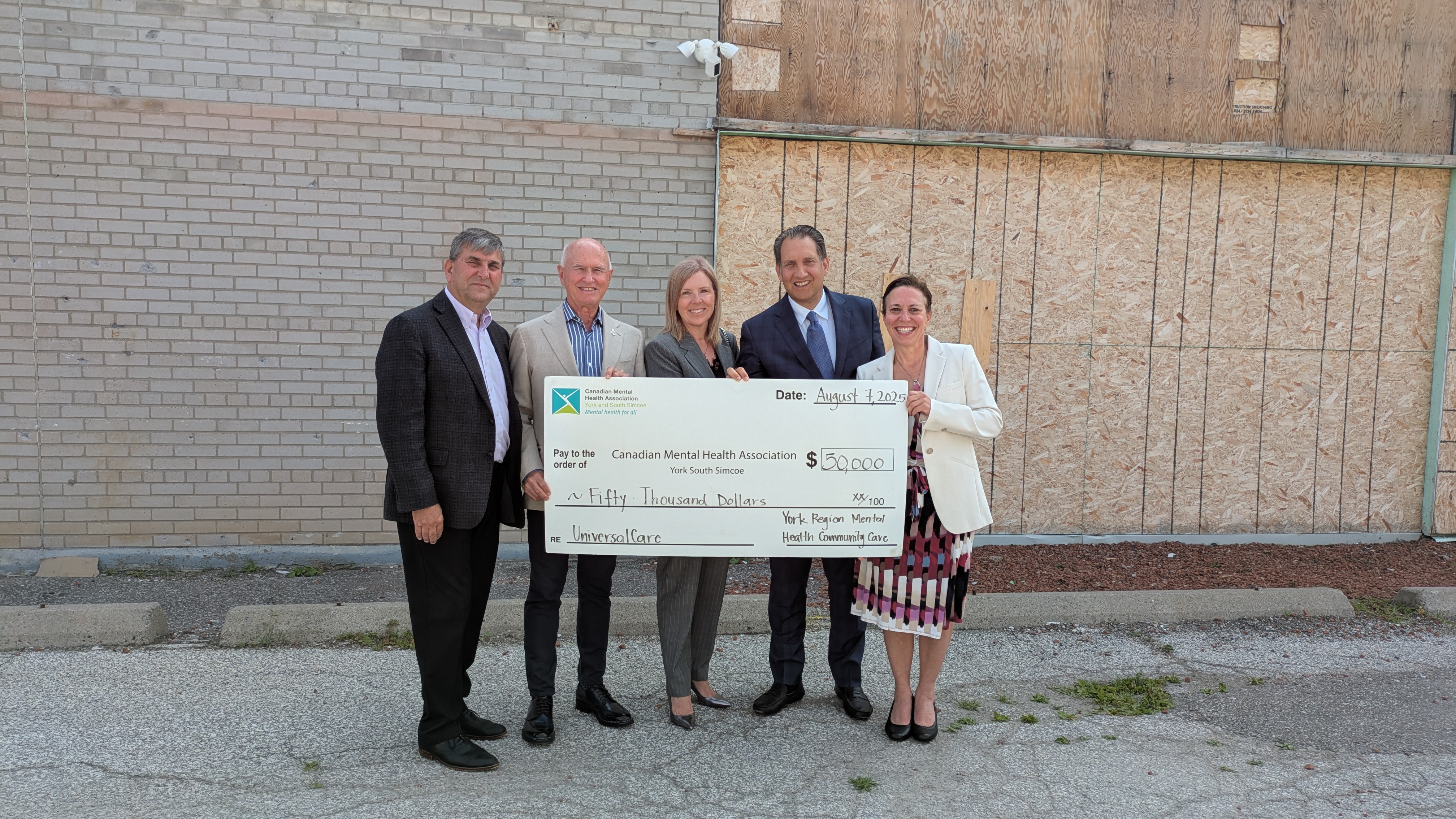 Men and women standing in front of a building holding a big cheque