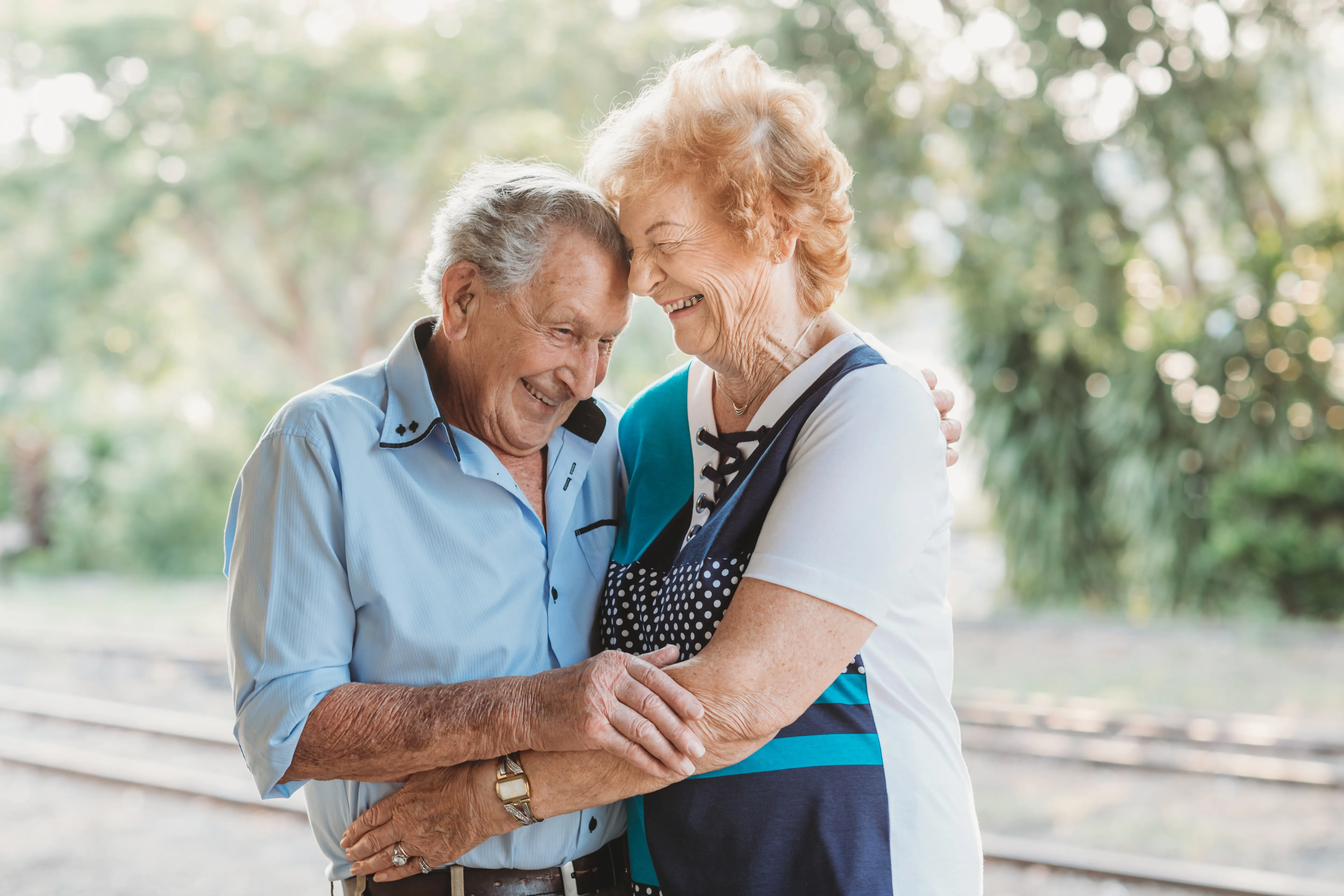 An elderly couple hugging outside.